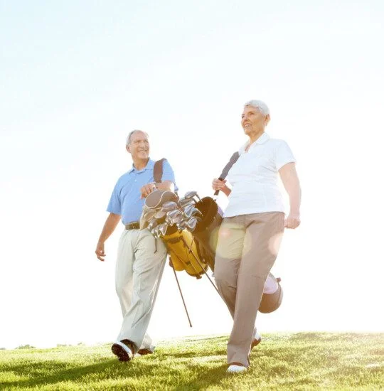 A happy senior couple walking along the fairway while carrying their golf bags