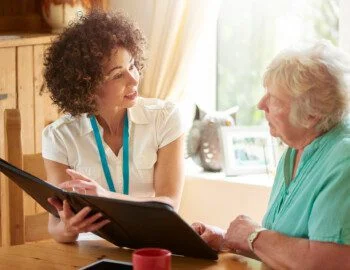 a care worker or medical professional or housing officer makes a house call to a senior client at her home . She is discussing the senior woman’s options on her digital tablet. a care worker or medical professional or housing officer makes a house call to a senior client at her home . She is discussing the senior woman’s options on her digital tablet.