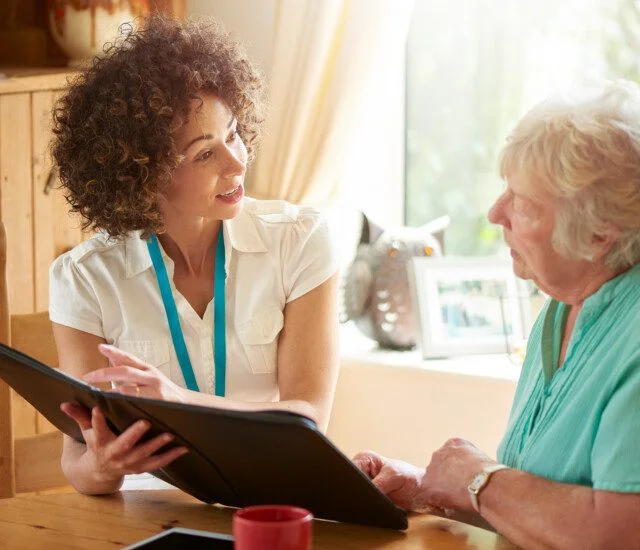 a care worker or medical professional or housing officer makes a house call to a senior client at her home . She is discussing the senior woman’s options on her digital tablet.