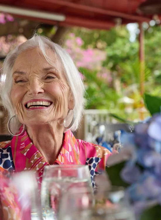 A close up of a senior woman smiling while eating lunch with friends