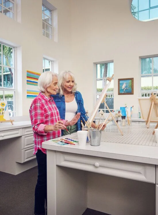 Two senior women painting and looking at a canvas
