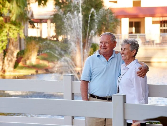 A senior couple standing on a bridge and look across the water