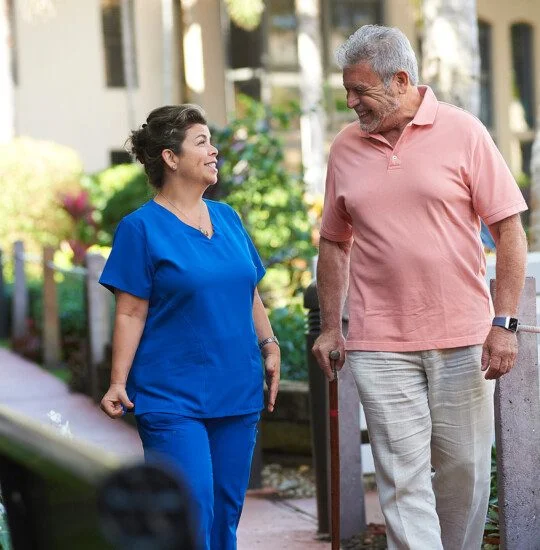 A senior man walking next to a skilled nurse