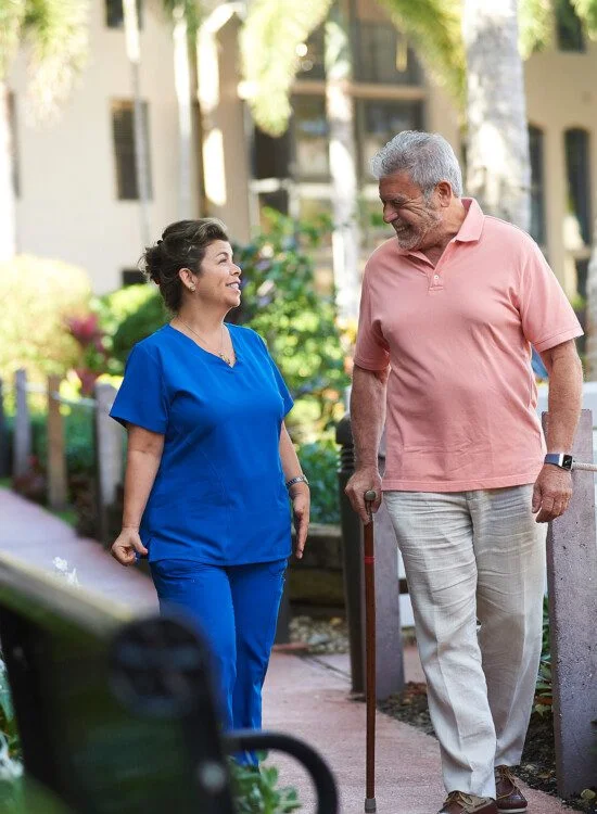 A senior man walking next to a skilled nurse