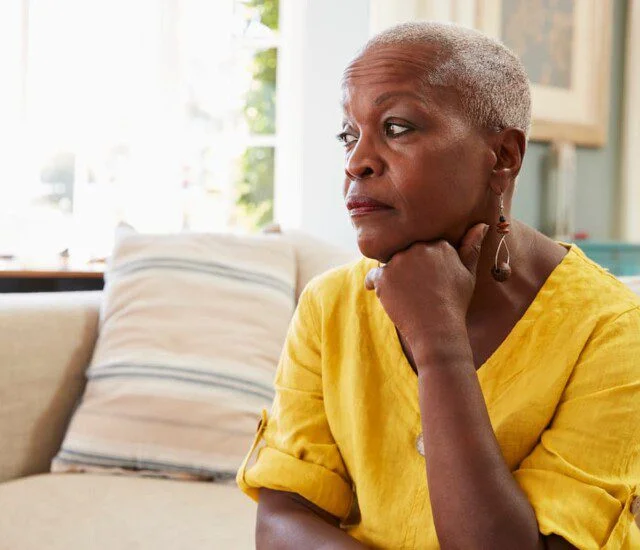 A senior woman sitting on a couch looking into the distance