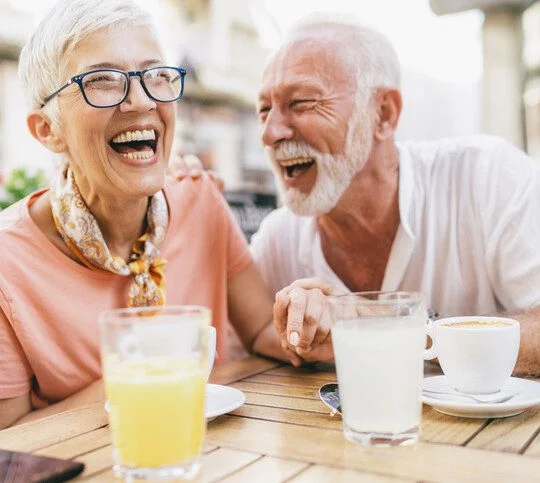 Older couple enjoying a laugh and a drink outside in the sun.