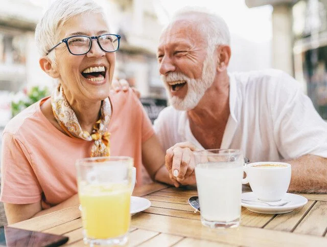 Older couple enjoying a laugh and a drink outside in the sun.