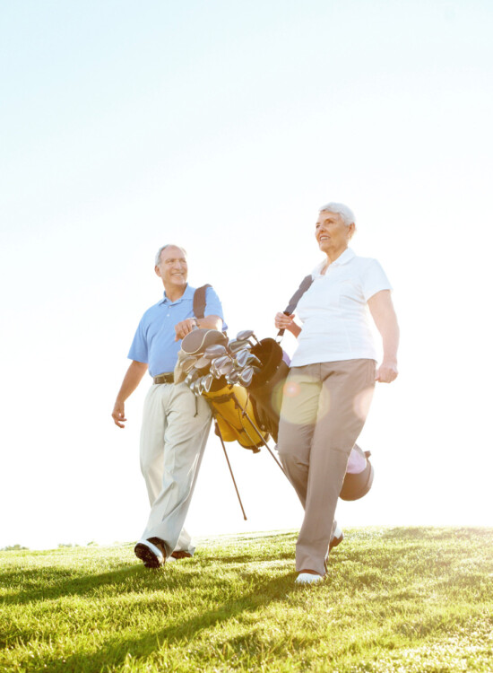 A happy senior couple walking along the fairway while carrying their golf bags