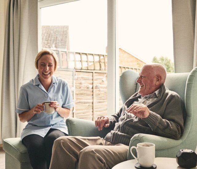 Indoor shot of smiling senior man and female enjoying coffee in living room