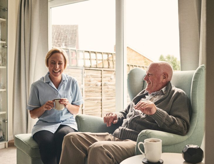 Indoor shot of smiling senior man and female enjoying coffee in living room