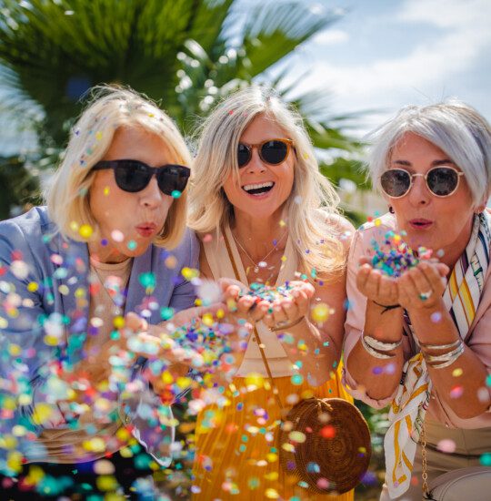 Fashionable mature friends having fun and celebrating by blowing colorful confetti in city street