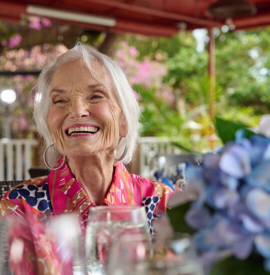 A close up of a senior woman smiling while eating lunch with friends