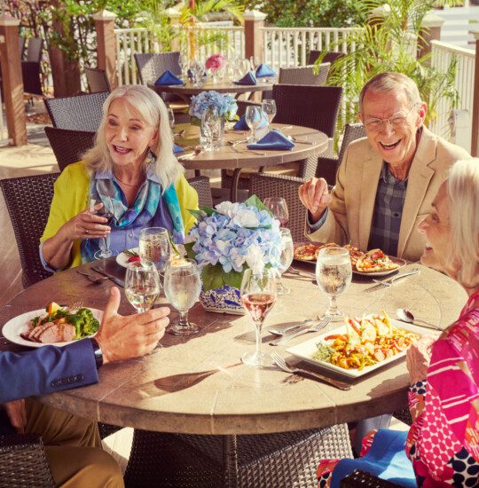 A group of seniors laughing and having lunch on a patio