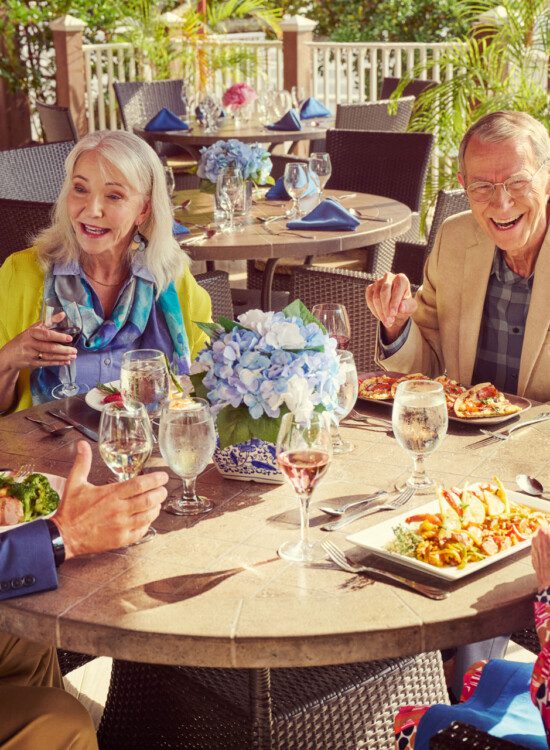 A group of seniors laughing and having lunch on a patio