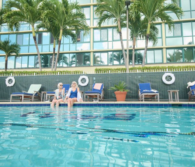 Two senior women laughing with their feet in the pool