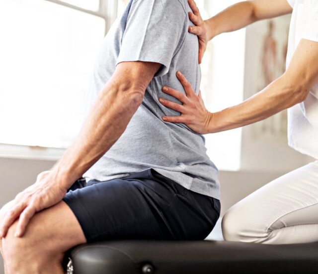 A senior man in rehab being helped to stretch his back