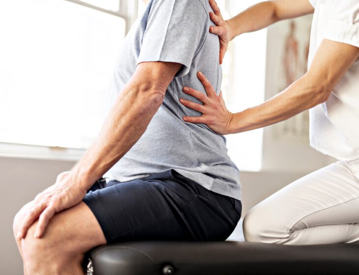 A senior man in rehab being helped to stretch his back