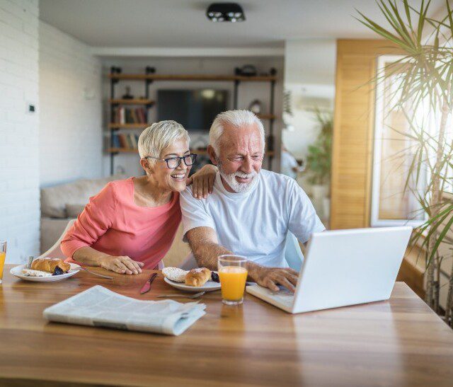 A senior couple smiling at a computer while eating breakfast