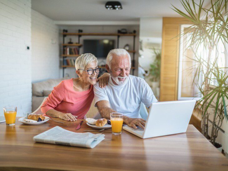 A senior couple smiling at a computer while eating breakfast