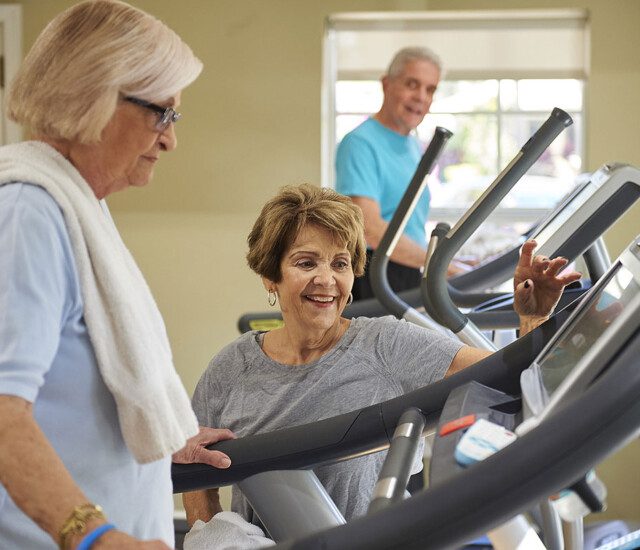 A senior woman on a treadmill talking to another woman