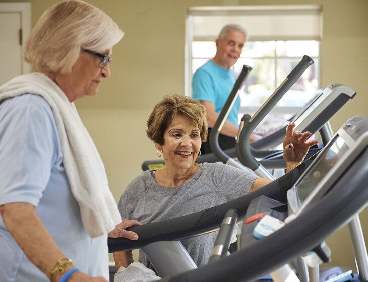 A senior woman on a treadmill talking to another woman