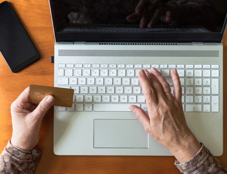 A senior holding their debit card while typing their information into a computer