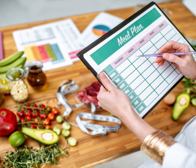 A woman holding a meal plan sheet with healthy food on the table