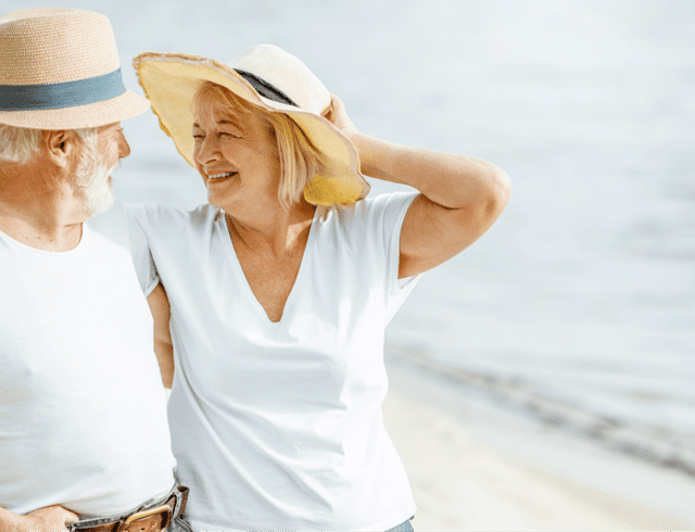 A senior couple in hats laughing on the beach