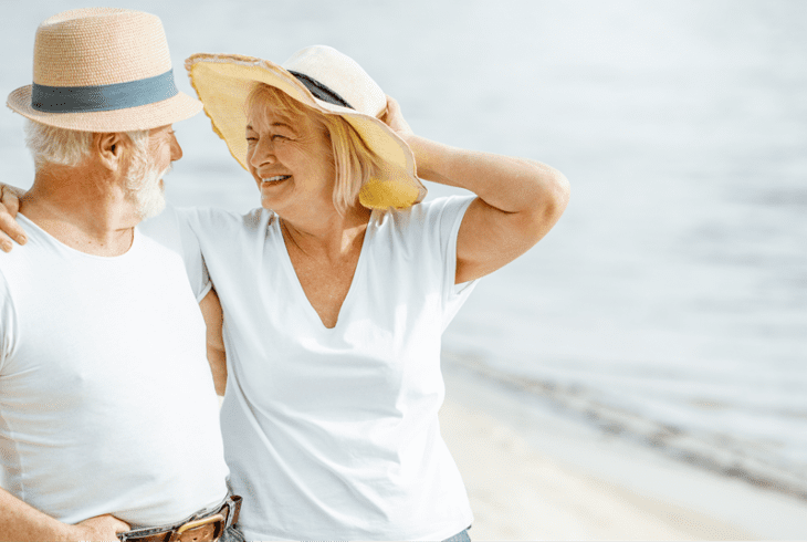 A senior couple in hats laughing on the beach