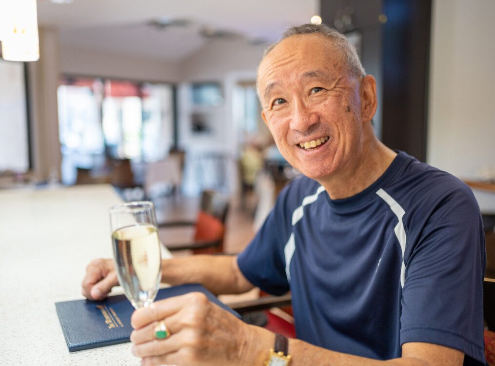 A senior man smiling with a menu and drink in his hand
