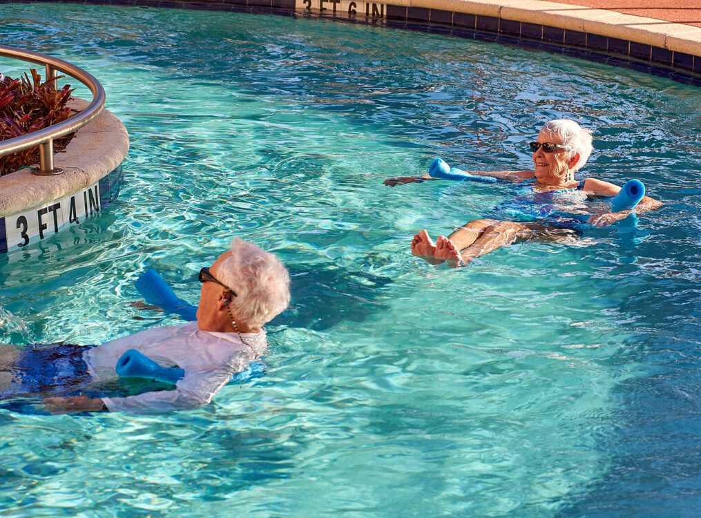 Two seniors floating in the pool with pool noodles