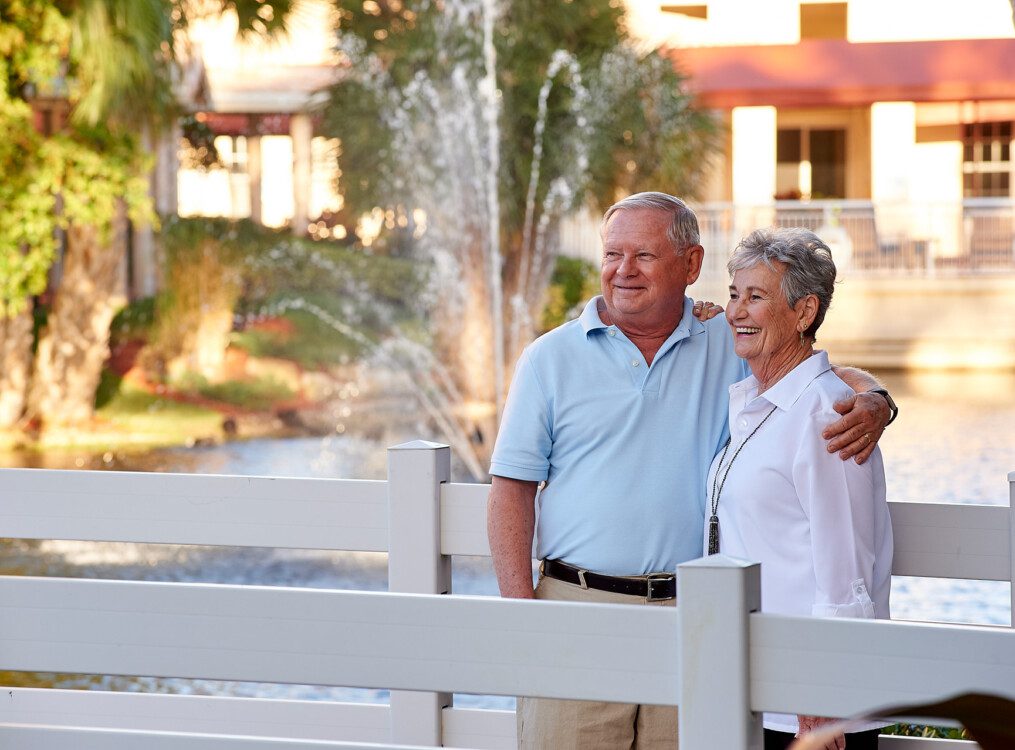 A senior couple standing on a bridge and look across the water