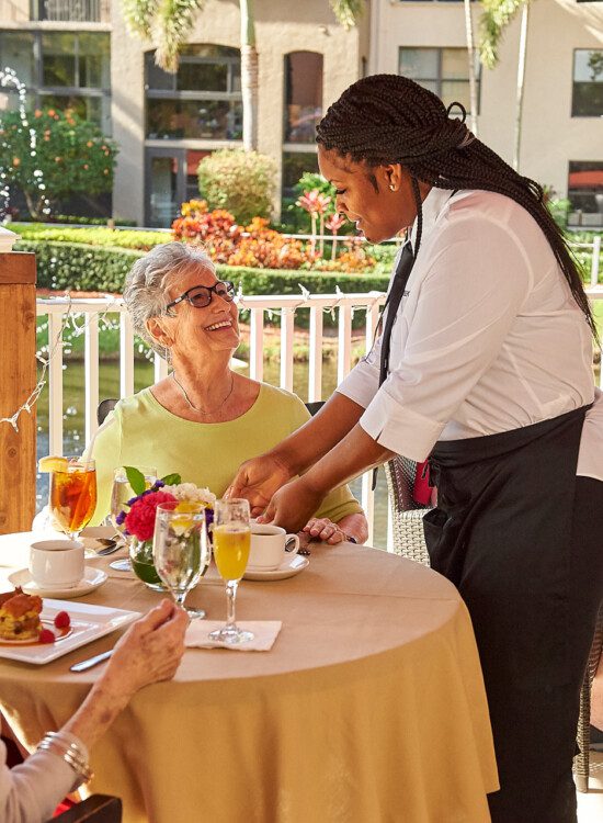 Old woman receives food from a server while having a meal with a friend