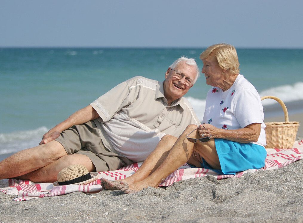 A senior couple laying on the beach laughing
