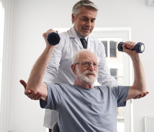 A senior man lifting weights with a helper assisting them