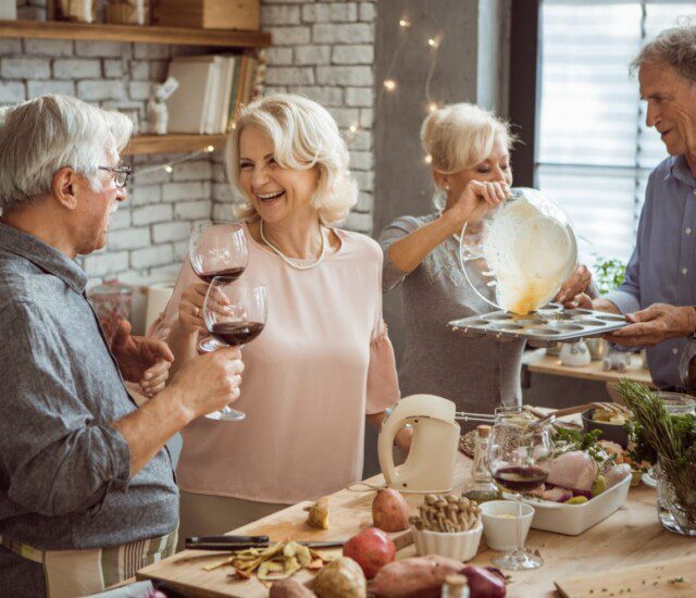 A group of seniors cooking and drinking wine together