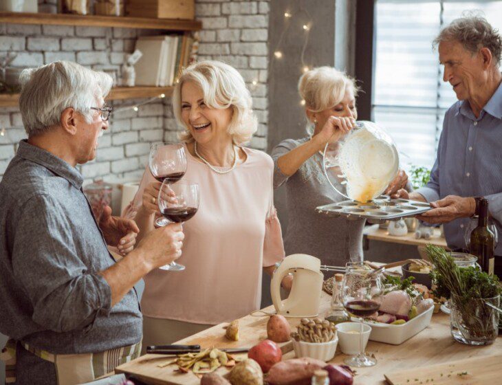 A group of seniors cooking and drinking wine together